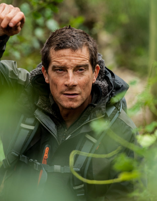 Bear Grylls standing among foliage and vegetation