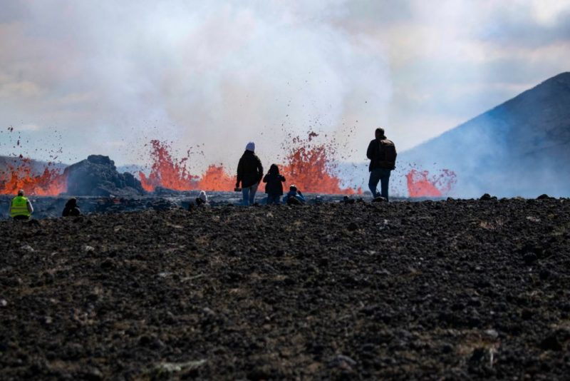 People standing in front of lava spewing from the Fagradalsfjall volcano