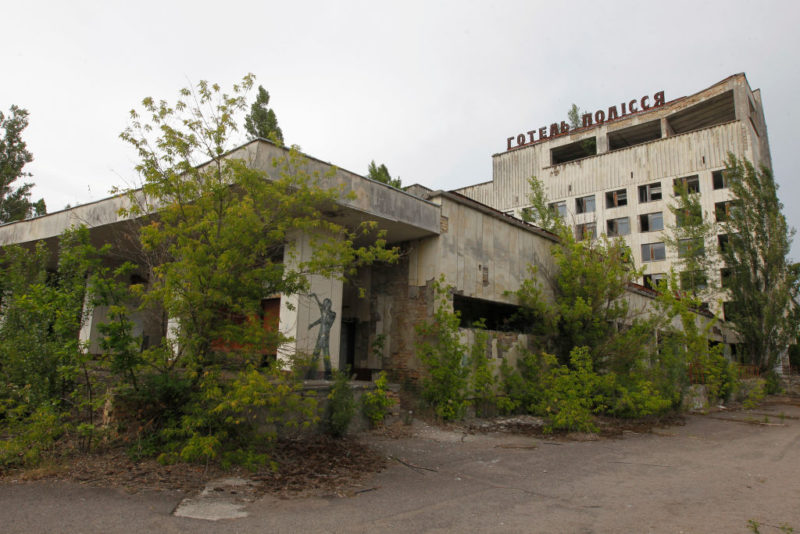 Exterior of a dilapidated hotel surrounded by trees and shrubs
