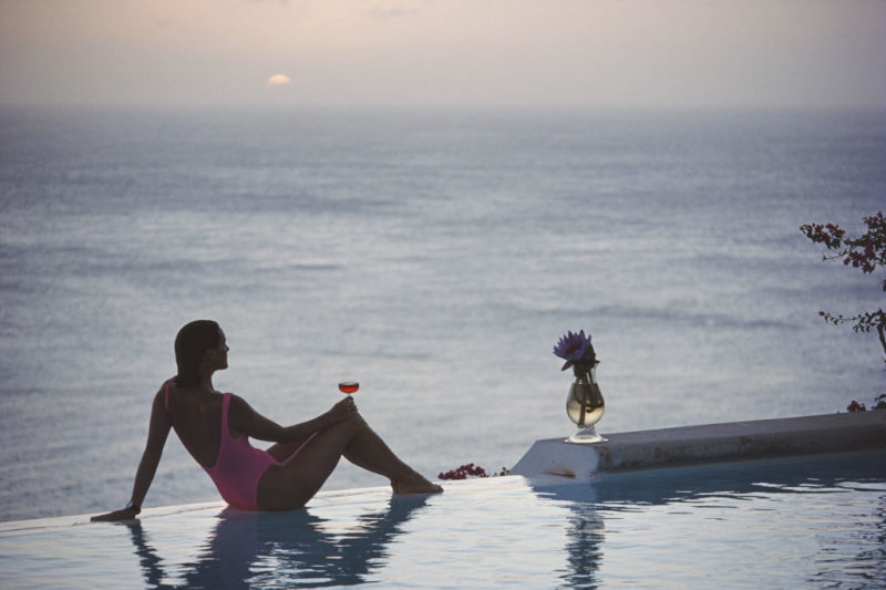 Woman sitting on the edge of a pool with a glass of wine