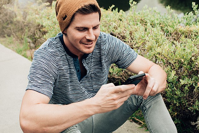 Man texting on his phone while sitting on the pavement