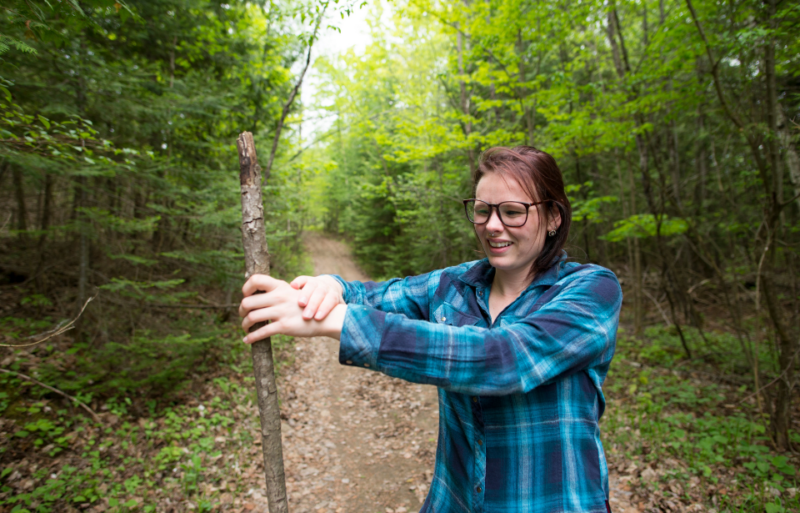 Woman holding a stick while standing along a woodland trail