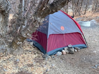 Rocks piled along the outside of a red and blue tent in the forest